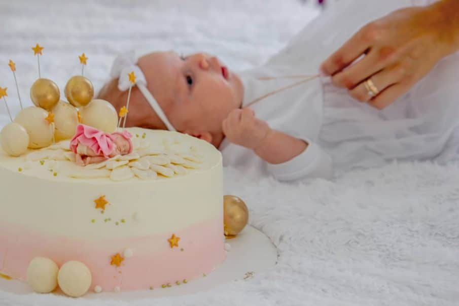 Fotograf roczek warszawa: zbliżenie na tort urodzinowy i detale sesji. Uroczy kadr z niemowlęciem w tle, idealny na pamiątkę pierwszych urodzin.