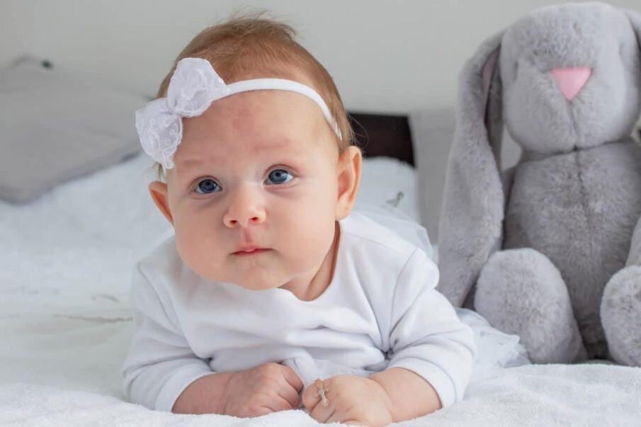 Fotograf reportaż chrzest warszawa: uroczy portret niemowlęcia w białej opasce. Kadr z dużym pluszowym królikiem, symbolizującym dzieciństwo i pamiątkę z sesji.