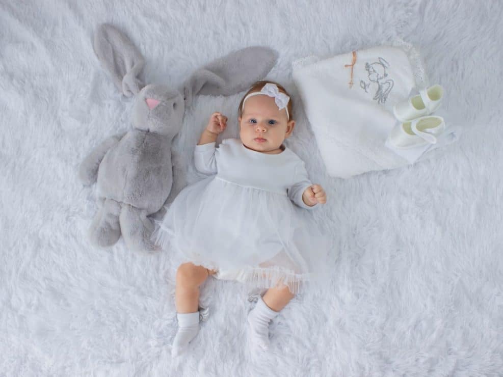 Fotograf chrzciny warszawa: zdjęcie niemowlęcia w ubranku do chrztu. Kadr ukazujący buciki, kocyk chrzcielny i rekwizyty – piękna pamiątka z chrztu.