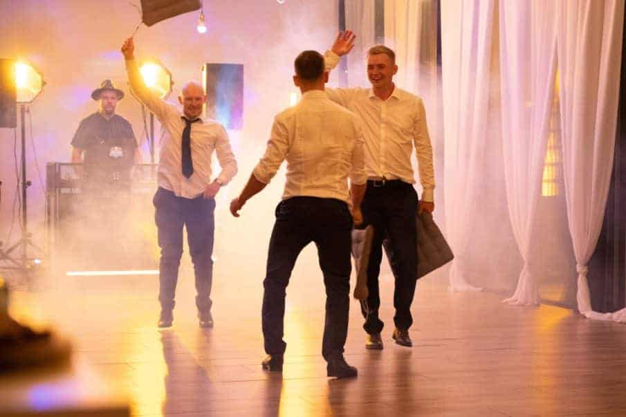 Ujęcie z imprezy okolicznościowej, goście tańczący obok stanowiska dja, efekt dymu na parkiecie.