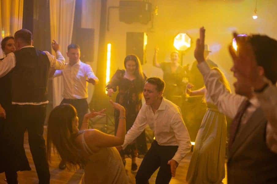 Ujęcie z imprezy okolicznościowej, ludzie śmiejący się i tańczący na parkiecie.