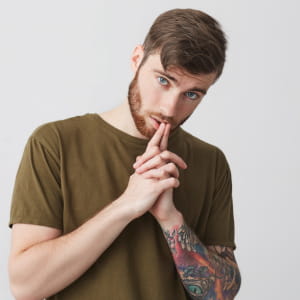 Autentyczne ujęcie mężczyzny z tatuażem na przedramieniu; zamyślona poza i skupione spojrzenie budujące intrygujący wizerunek w sieci.