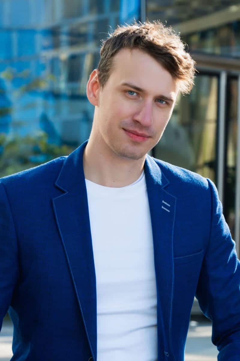 Mężczyzna w niebieskiej marynarce i białym t-shircie uśmiecha się na zewnątrz. Przykład, jakie zdjęcia na tindera budują wizerunek smart-casual dla mężczyzn w warszawie
