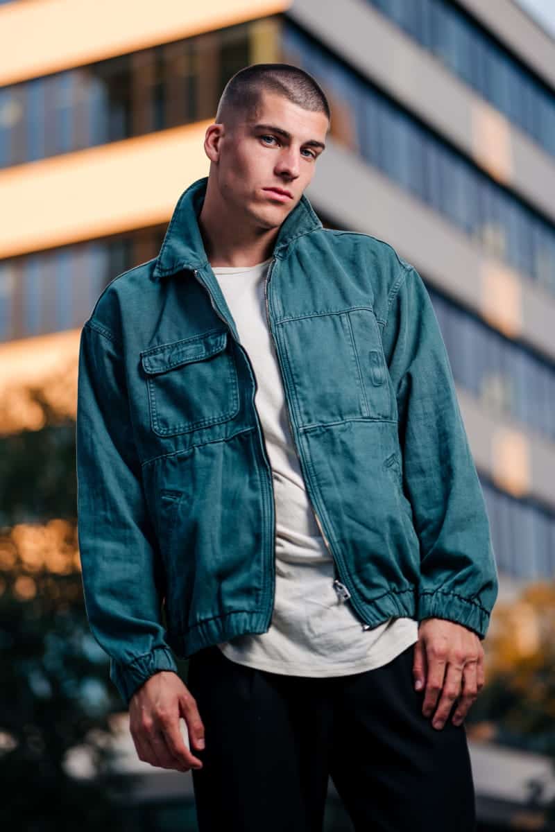 Nowoczesna sesja uliczna dla mężczyzny. Młody mężczyzna w zielonej kurtce na tle biurowca profesjonalny fotograf