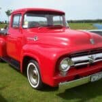 Red 1956 Ford F-100 pickup showing its wraparound windshield