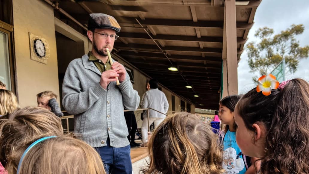 Quin Herron playing tin whistle with school children watching.