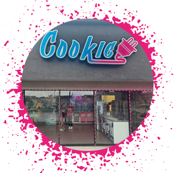 Gray storefront with a pink, purple, and blue gradient sign that says 'Cookie' with an electrical plug attached to it with graffiti and an alligator in the window.