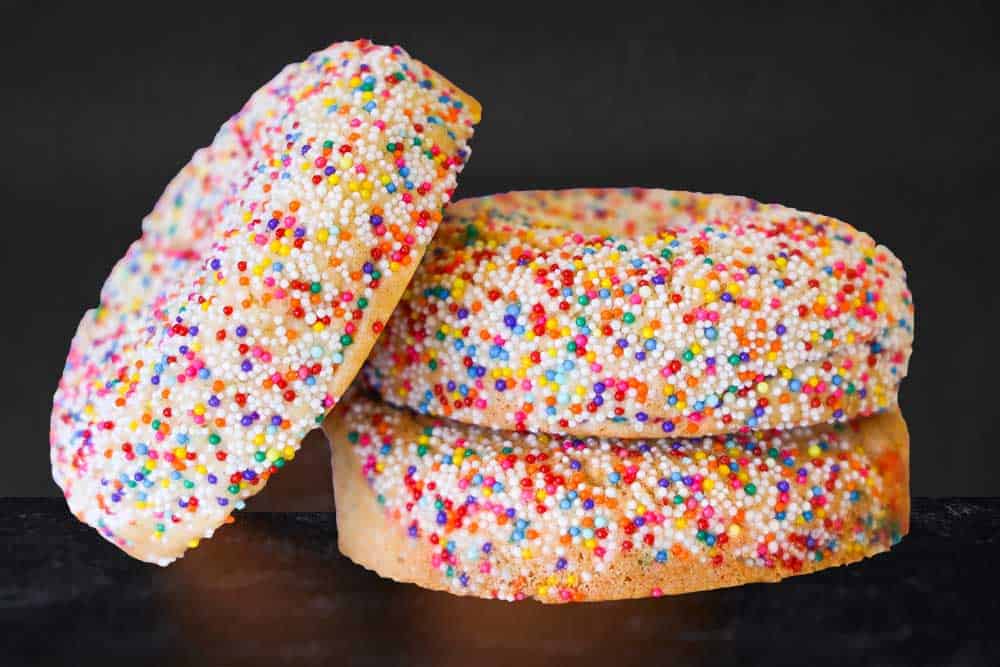 A stack of three thick cookies with rainbow sprinkles with a dark gray background