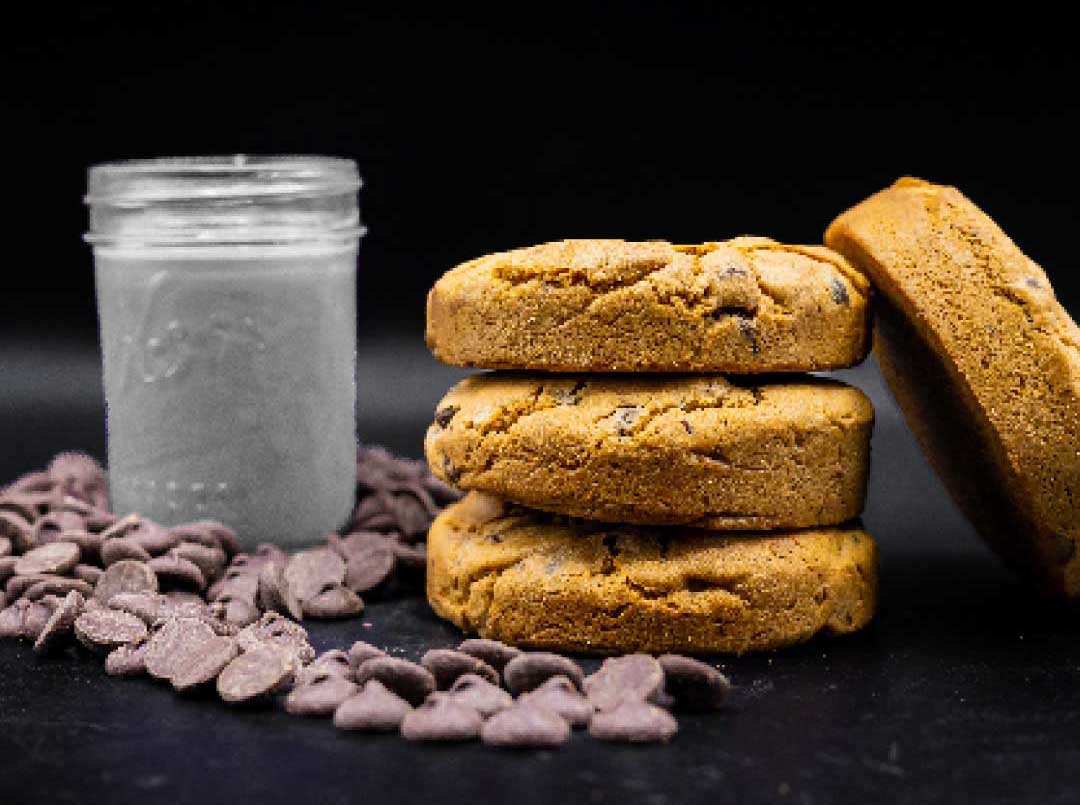 4 thick chocolate chip cookies with scattered dark chocolate chips with a glass of milk.