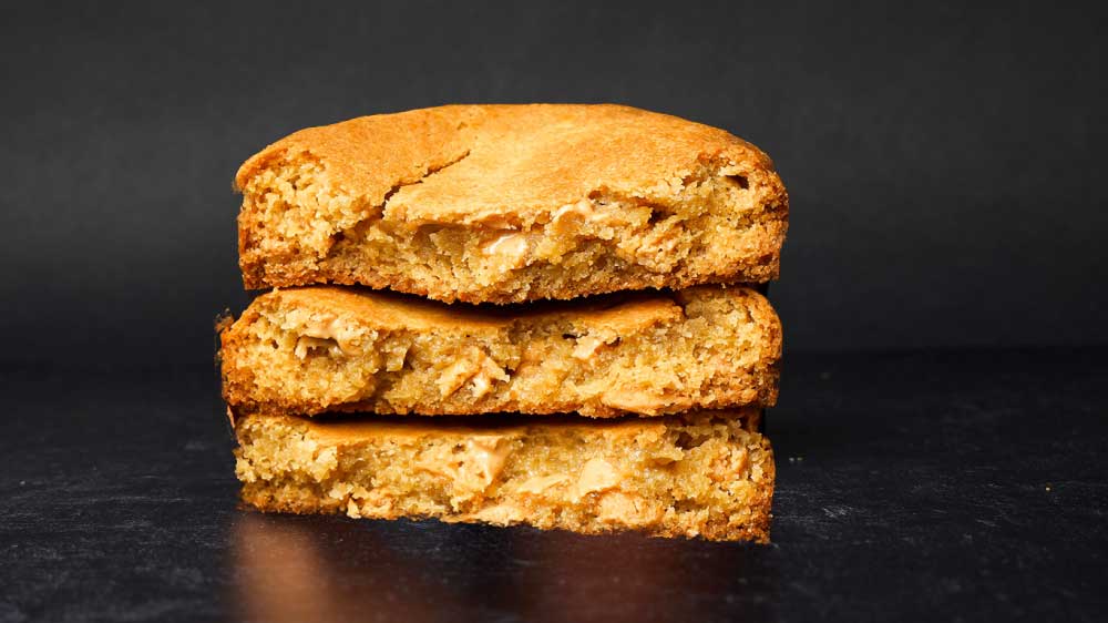 A stack of three thick peanut butter cookies that are sliced open on a back background