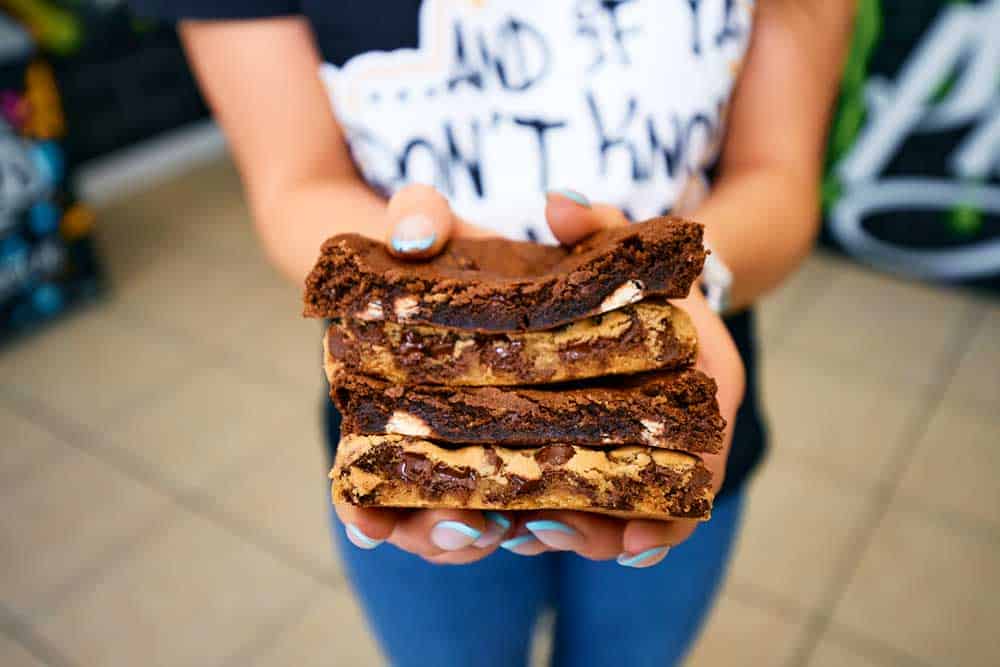 Thick stacks of cookies with chocolate with white chocolate chips and regular thick chocolate chip cookies with a girl who has baby blue nails.