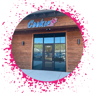 Circular image of wooden building with large black glass windows and doors with a big blue sign that says 'cookie' with a pink electrical plug attached to it that has a pink spray paint trip border