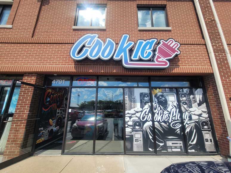 Brick storefront with a large black and white graffiti mural with Biggie, sitting on speakers with cookies all around him.