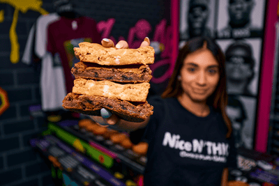 Girl out of focus who is hold a thick stack of cookies in various flavors like chocolate chip cookie and cookies with white chocolate chips.