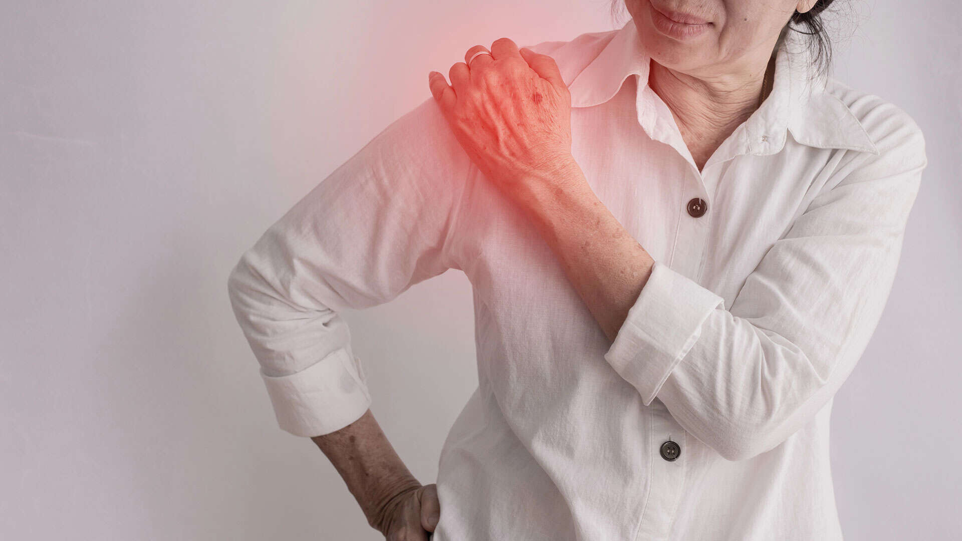 An older woman in a white shirt holds her left shoulder, which is highlighted in red, suggesting pain or discomfort and the possible need for pain management.