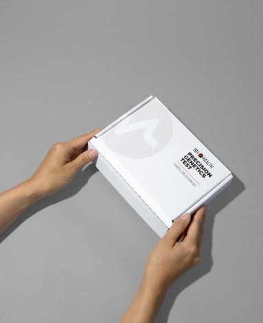 Two hands hold a white box labeled "Precision Prevention Test" on a plain gray background.