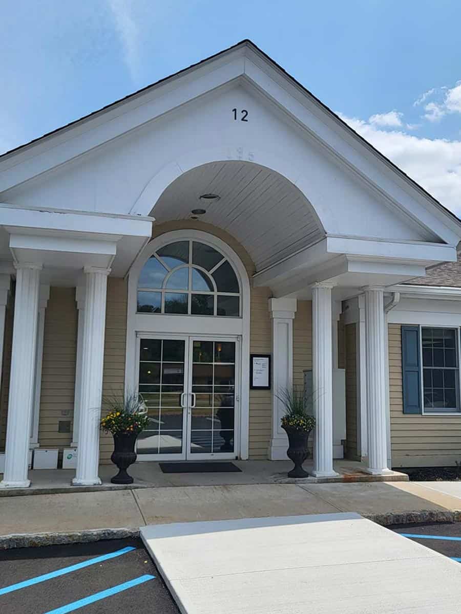 A beige building with white columns, a glass double door entrance, two potted plants, and the number 12 above the arched entryway.