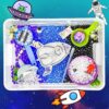 Space-themed craft kit spread across a transparent tray with beads, tools, and decorations, plus a cartoon UFO and astronaut clip art in the background.