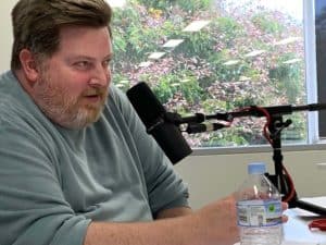 Bearded man in front of microphone looking toward a guest out of shot