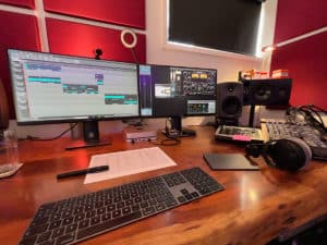 podcast production studio desk showing computer monitors running audio editing software. 