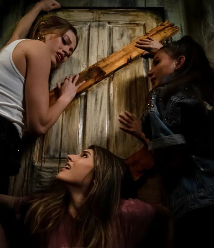 Three women are standing in front of a wooden door.