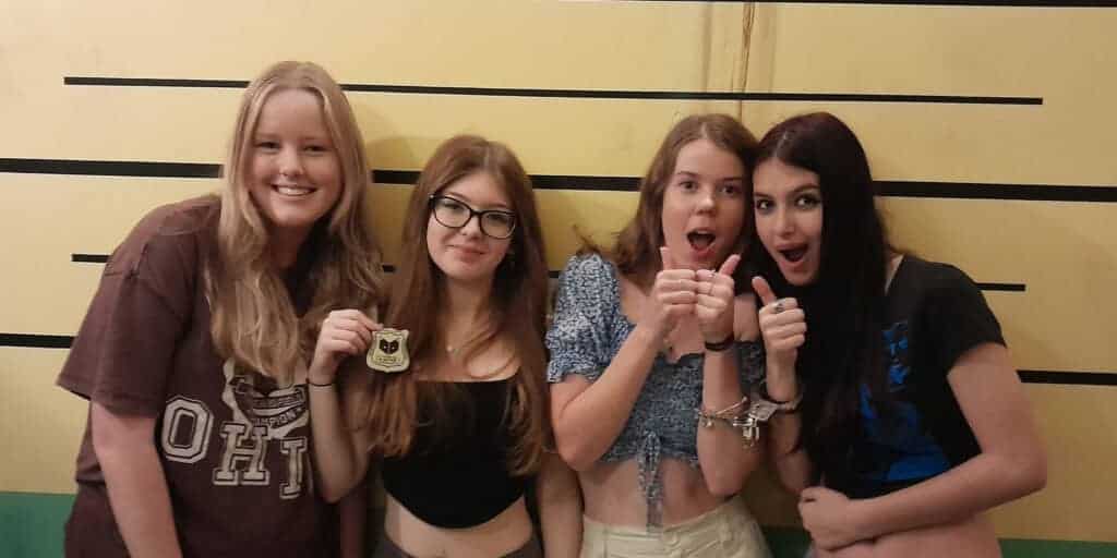 Four girls posing for a picture in front of a jail cell.