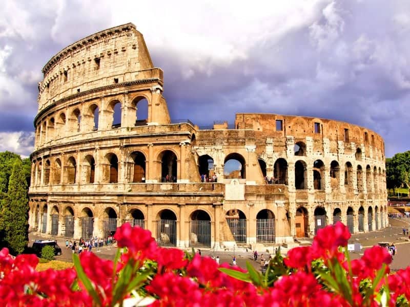 The Colosseum in the background with cloudy sky and bright red flowers in the foreground