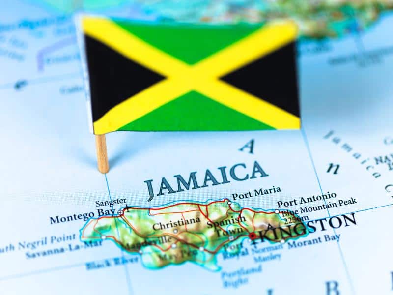 Map of Jamaica with miniature flag showing the vibrant green, black, and gold colors of the Jamaican national flag pinned to its location in the Caribbean Sea