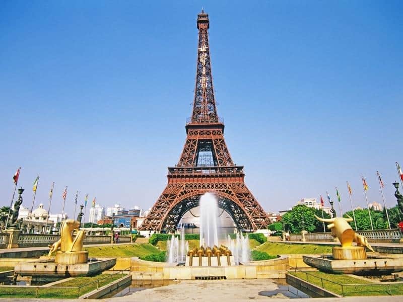 Full view of the Eiffel Tower in Paris with fountains and gardens in the foreground on a clear day