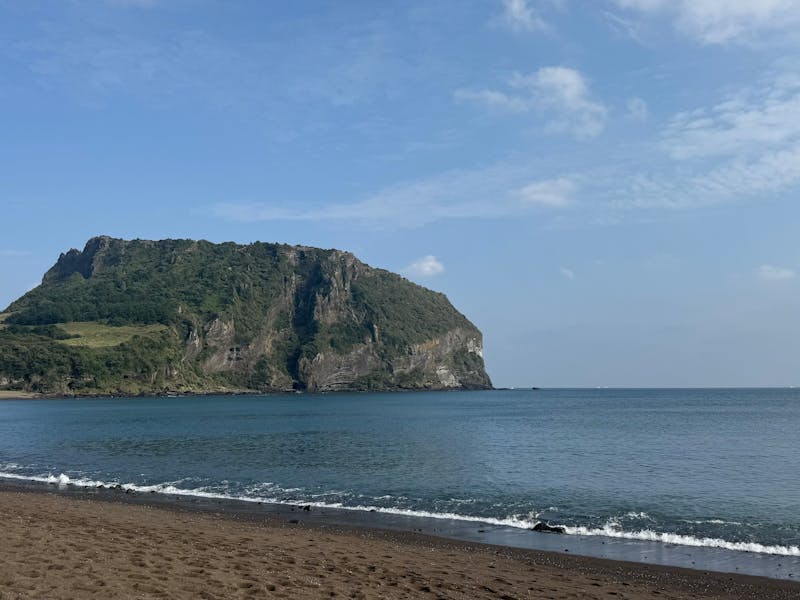 Peaceful beach view with Seongsan Ilchulbong peak on Jeju Island, South Korea.