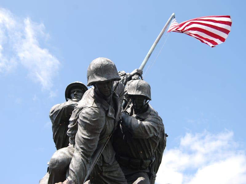 Dramatic view of the Iwo Jima Memorial under a blue sky, featuring US Marines raising the American flag.