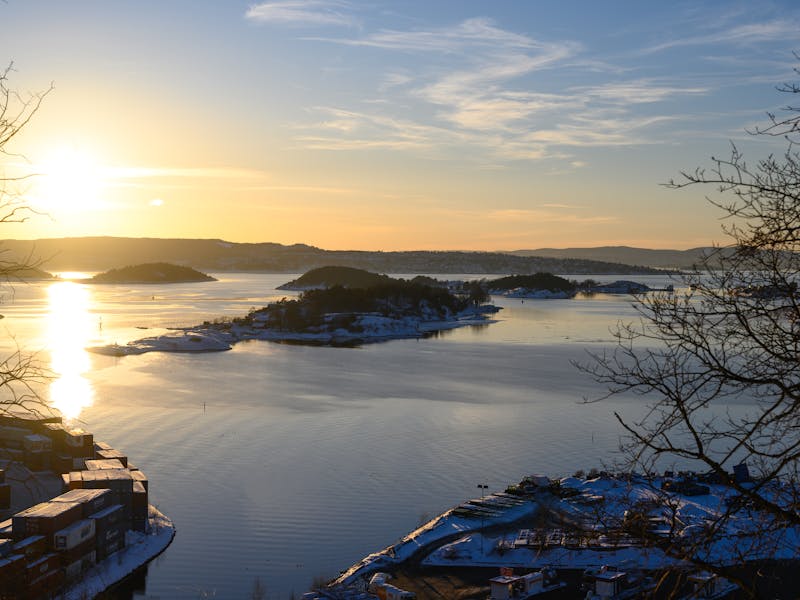 A beautiful winter sunset over Oslo Fjord, highlighting islands and a calm sea with silhouetted trees.