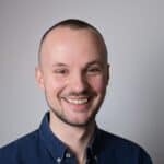 Philipp Goetza lächet in die Kamera. Er hat braune Augen, sehr kurze braune Haare und trägt ein dunkelblaues Jeans-Hemd.