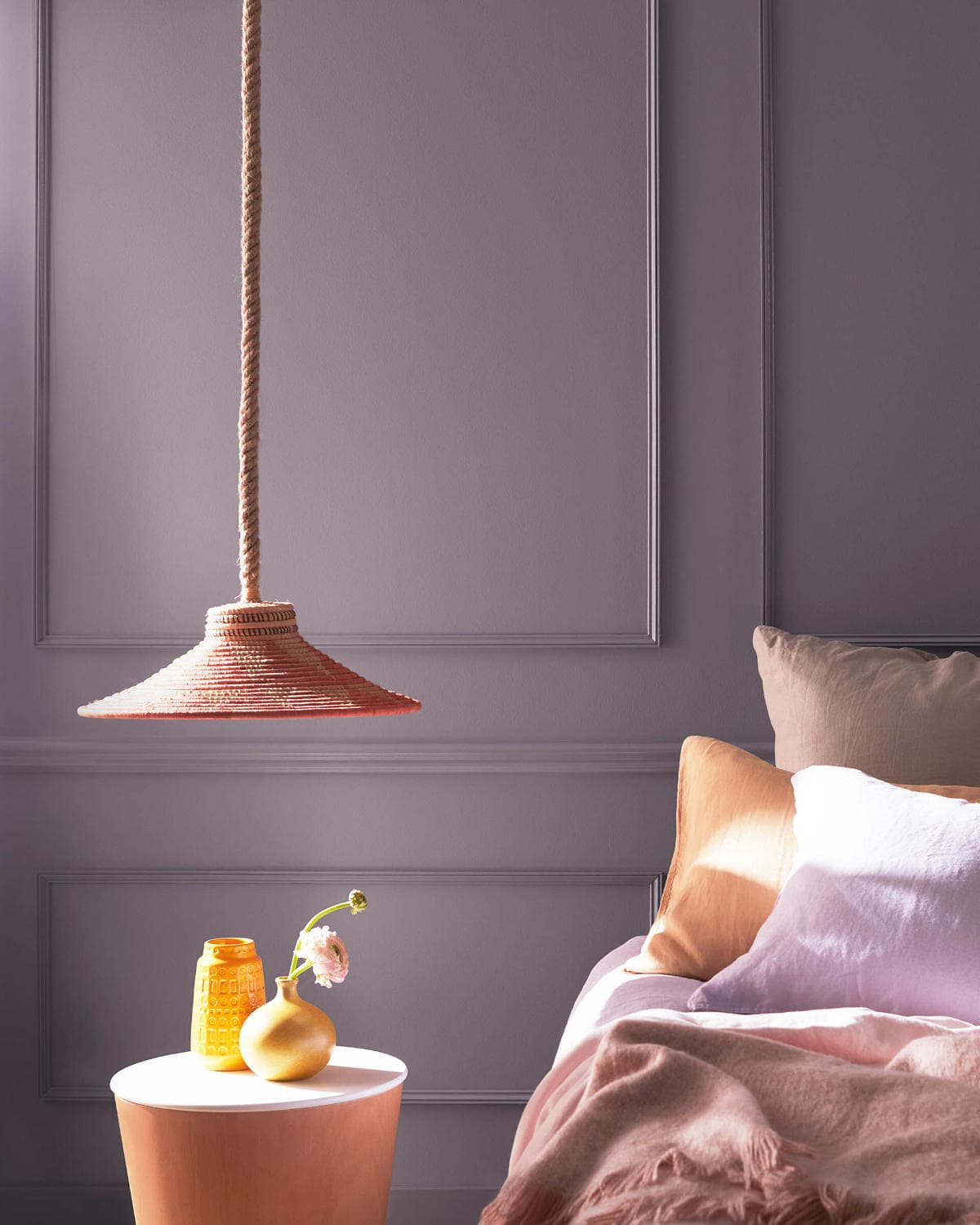 hazy-lilac-benjamin-moore-colour wall painted with benjamin moore hazy lilac colour in a room with a bed, small table, and lamp.