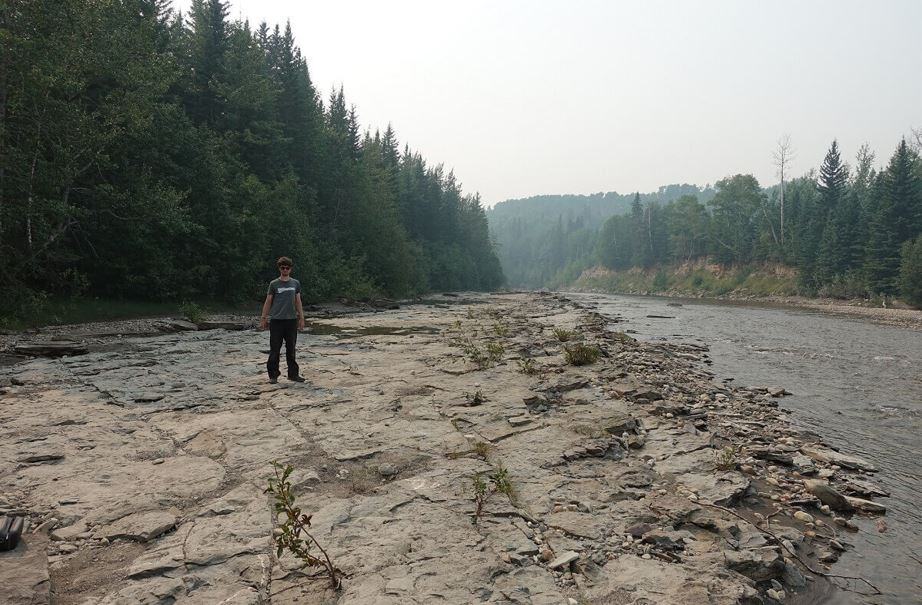 Man standing on river bed with trees in background