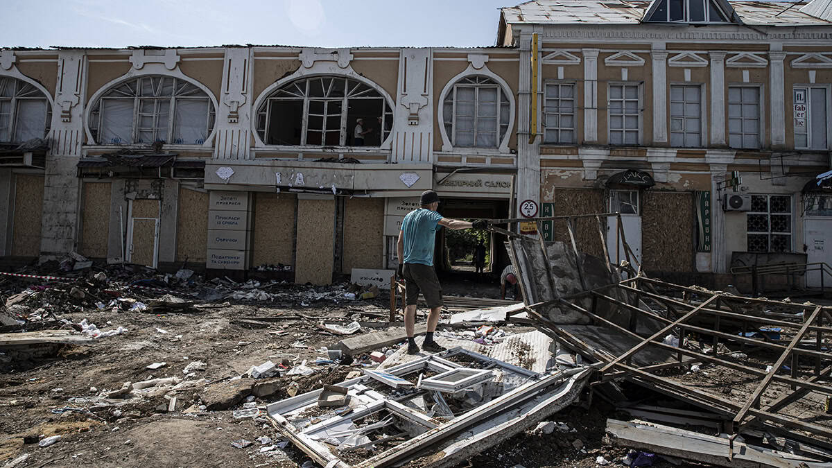 Man facing away from the camera on a pile of rubble looking at a damaged building in the background