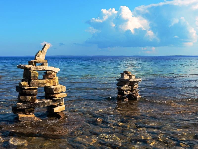 Two inuksuit (piles of rocks resembling a human figure) in the shallow water near the coast of Lake Huron