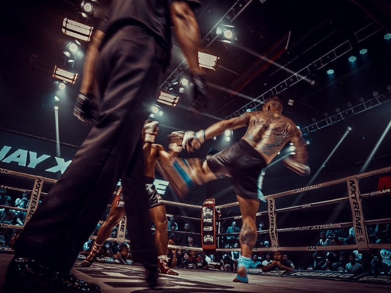 Two muay thai fighters in a ring in Bangkok, with a ref standing to the side