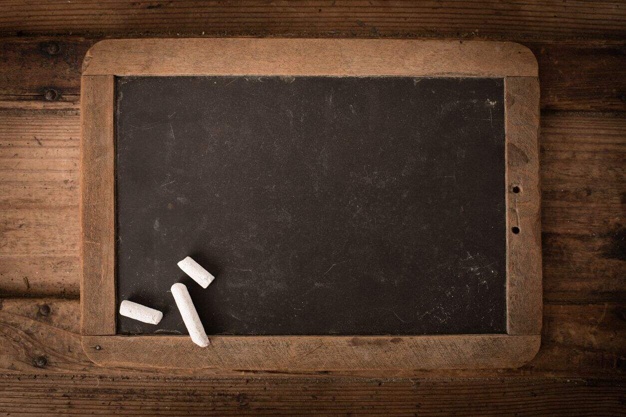 Antique Slate Chalkboard with Wood Frame on Old Trunk Color stock photo of an old, well-used school slate chalkboard with wood frame and chalk sitting on an old wooden trunk.