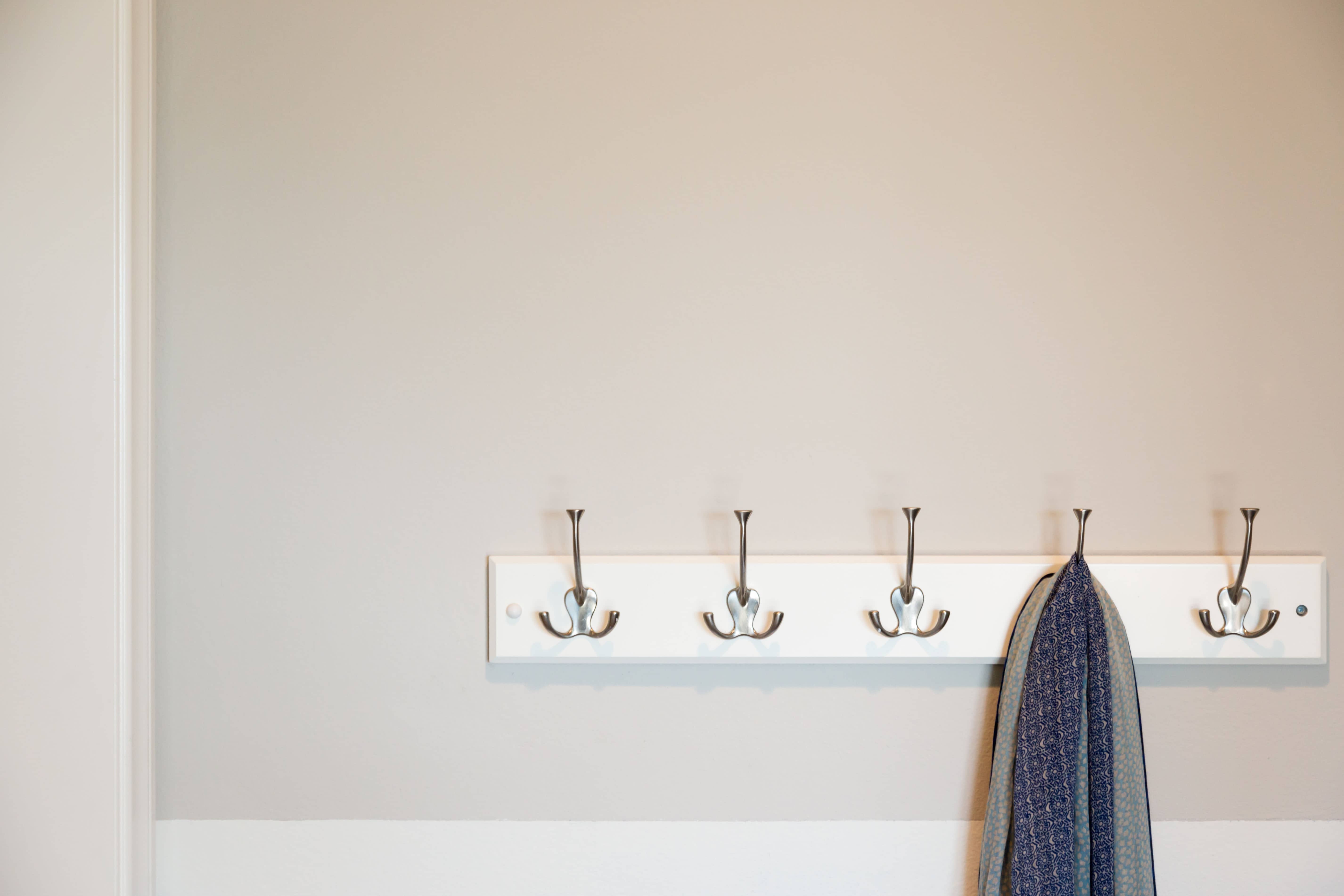 A row of polished wall hooks mounted on a plain painted wall, with a single dark wool coat hanging from one hook.