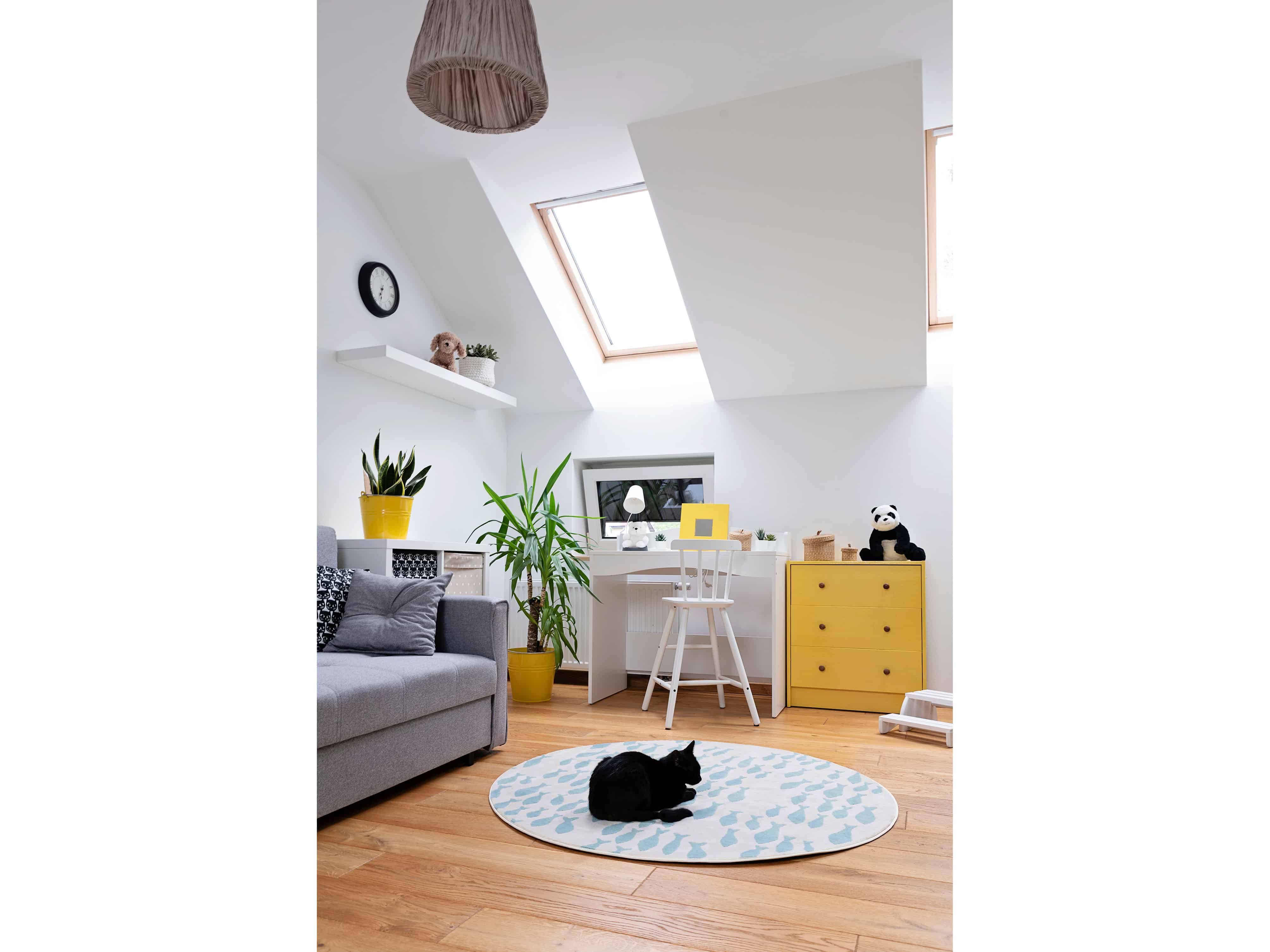 A mustard-yellow low cabinet and open shelving tuck neatly under a sloped attic ceiling, with a small desk nook fit into the eave beside it.