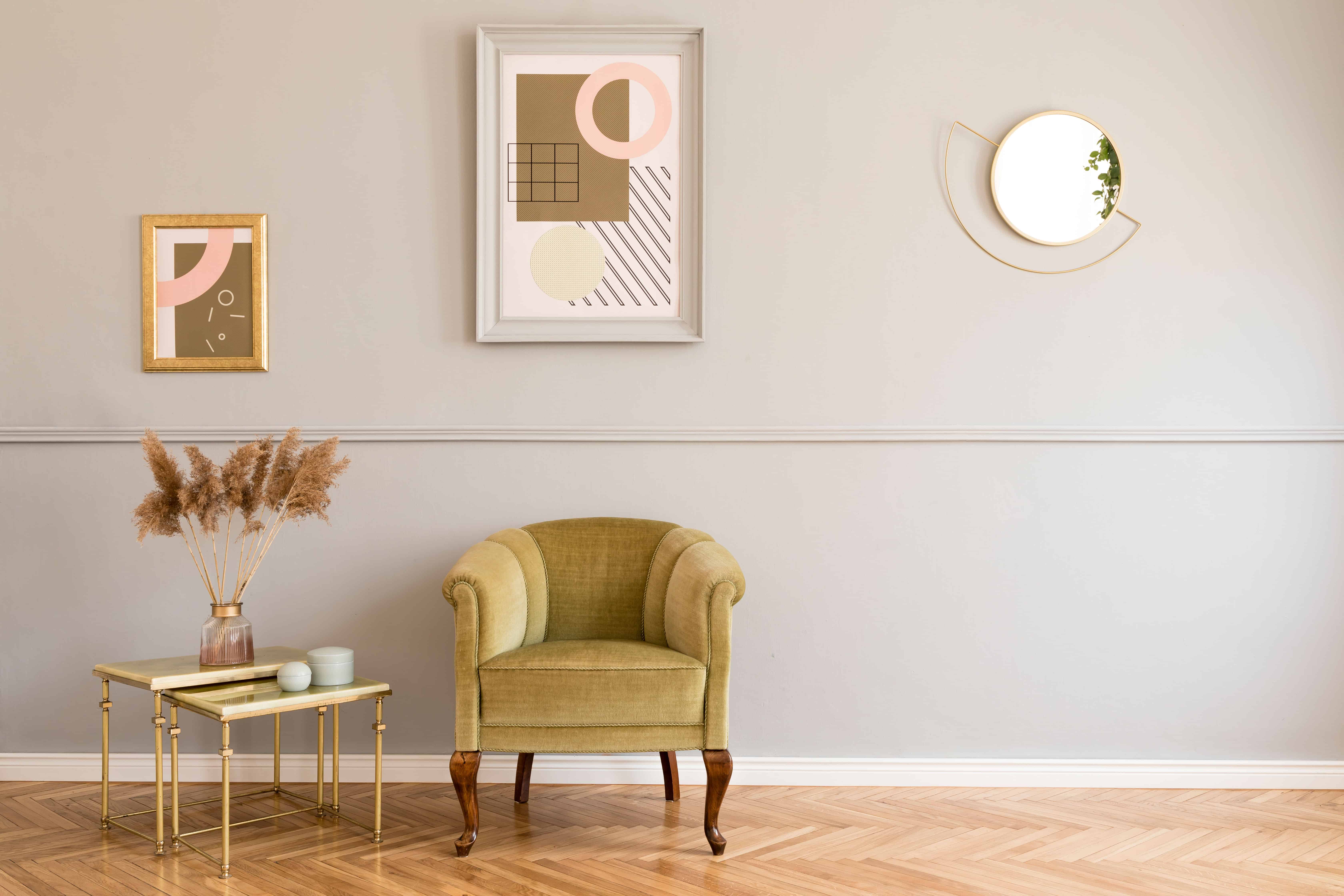 An emerald-green velvet armchair sits beside a round brass side table in a richly styled living room corner with gallery art and a mirror.