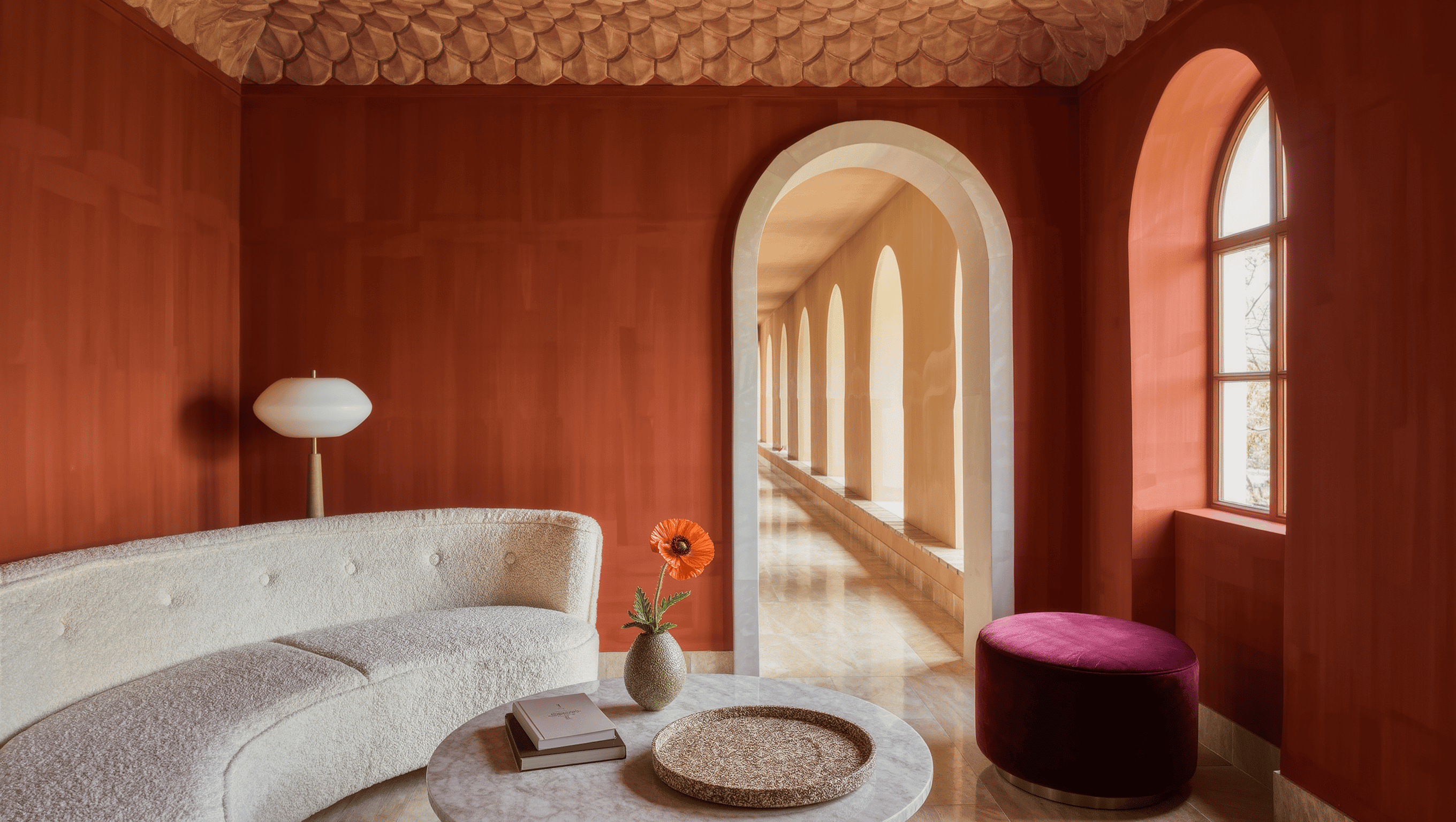 A room with an arched doorway, curved ivory boucle sofa, round travertine table, scalloped ceiling detail, and warm arched-window daylight.