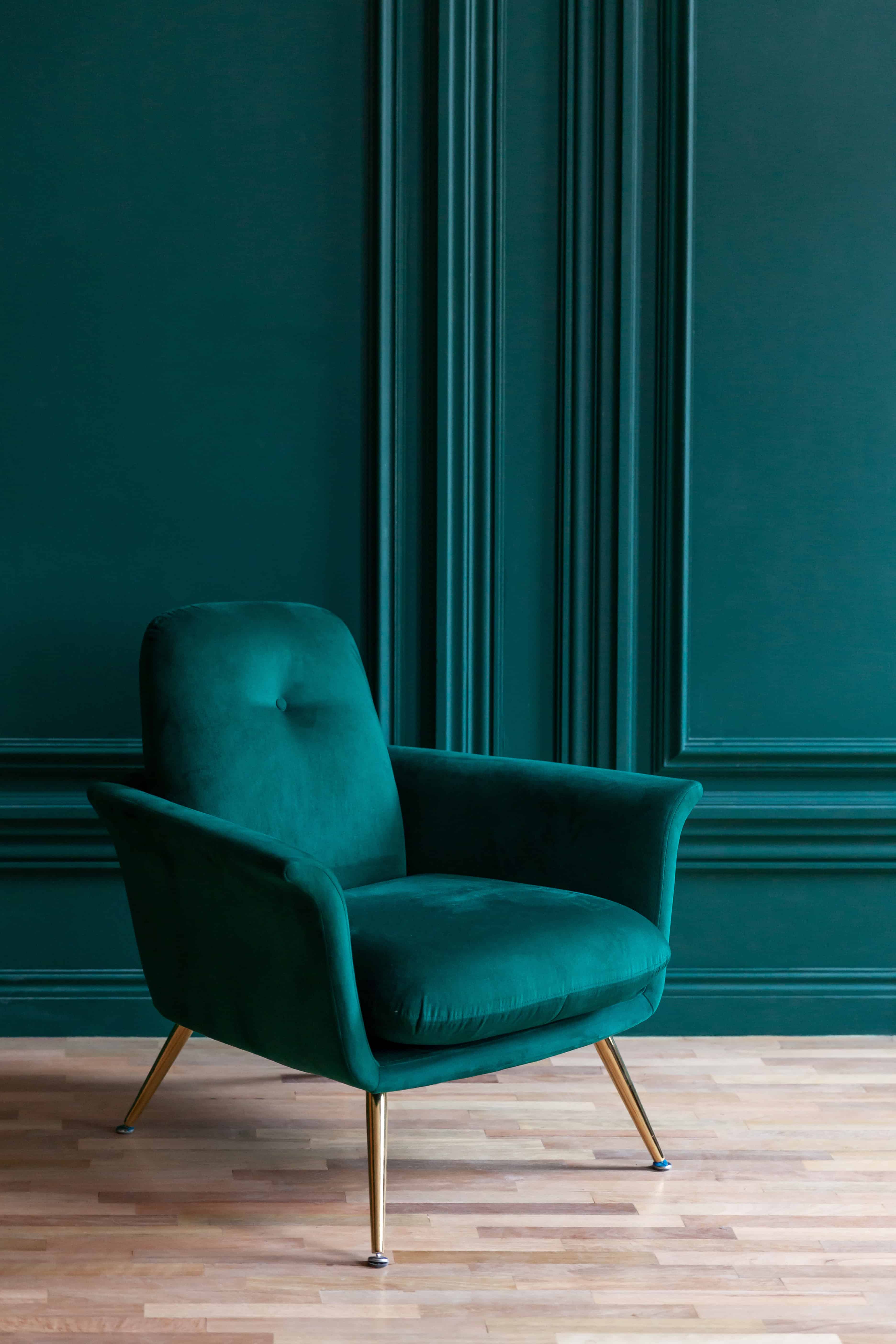 A single deep emerald velvet armchair with slim brass legs stands against a matching green paneled wall.