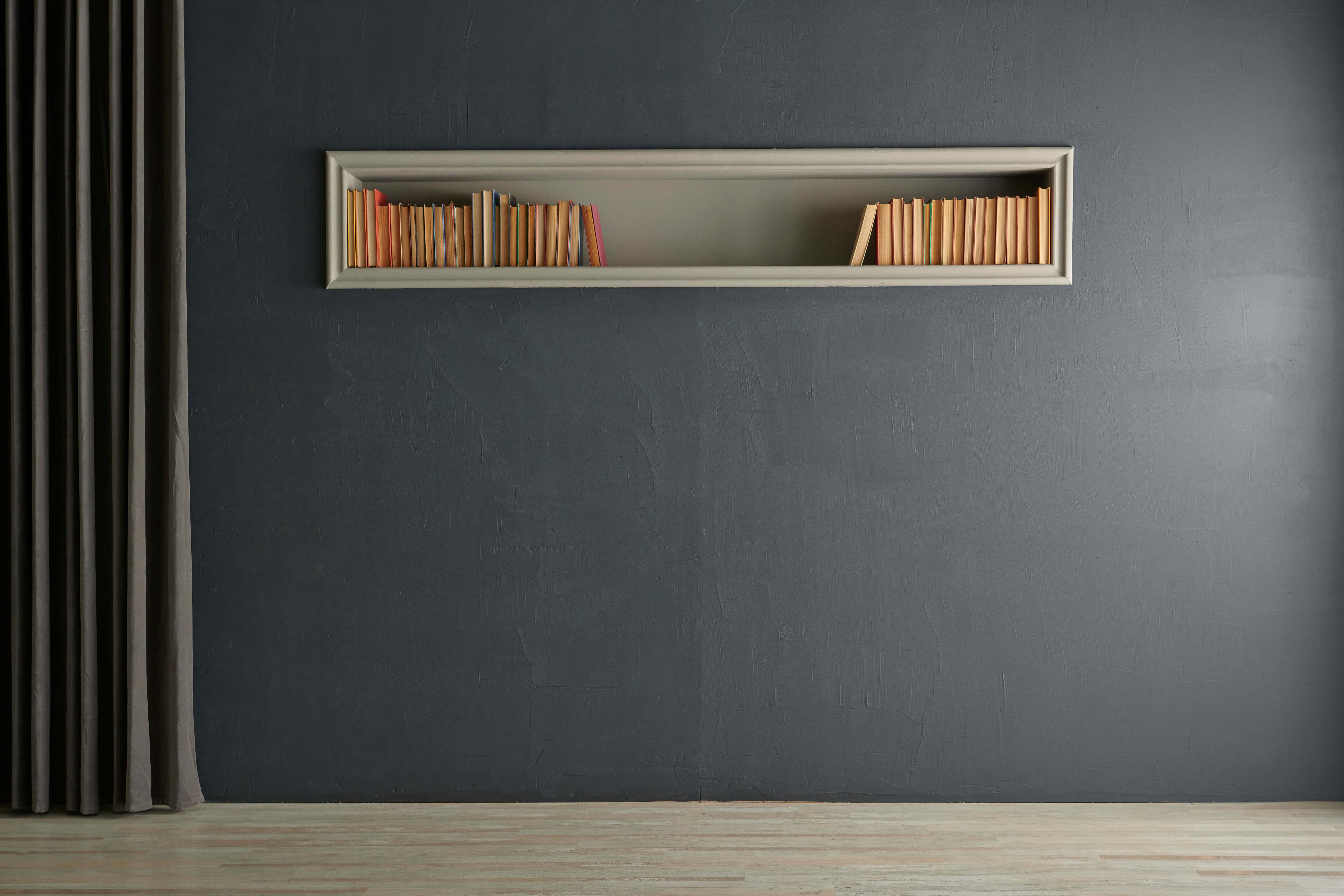 A long built-in niche cut into a charcoal-grey wall is framed with a slim molding and styled with rows of books, giving the shallow recess quiet presence.