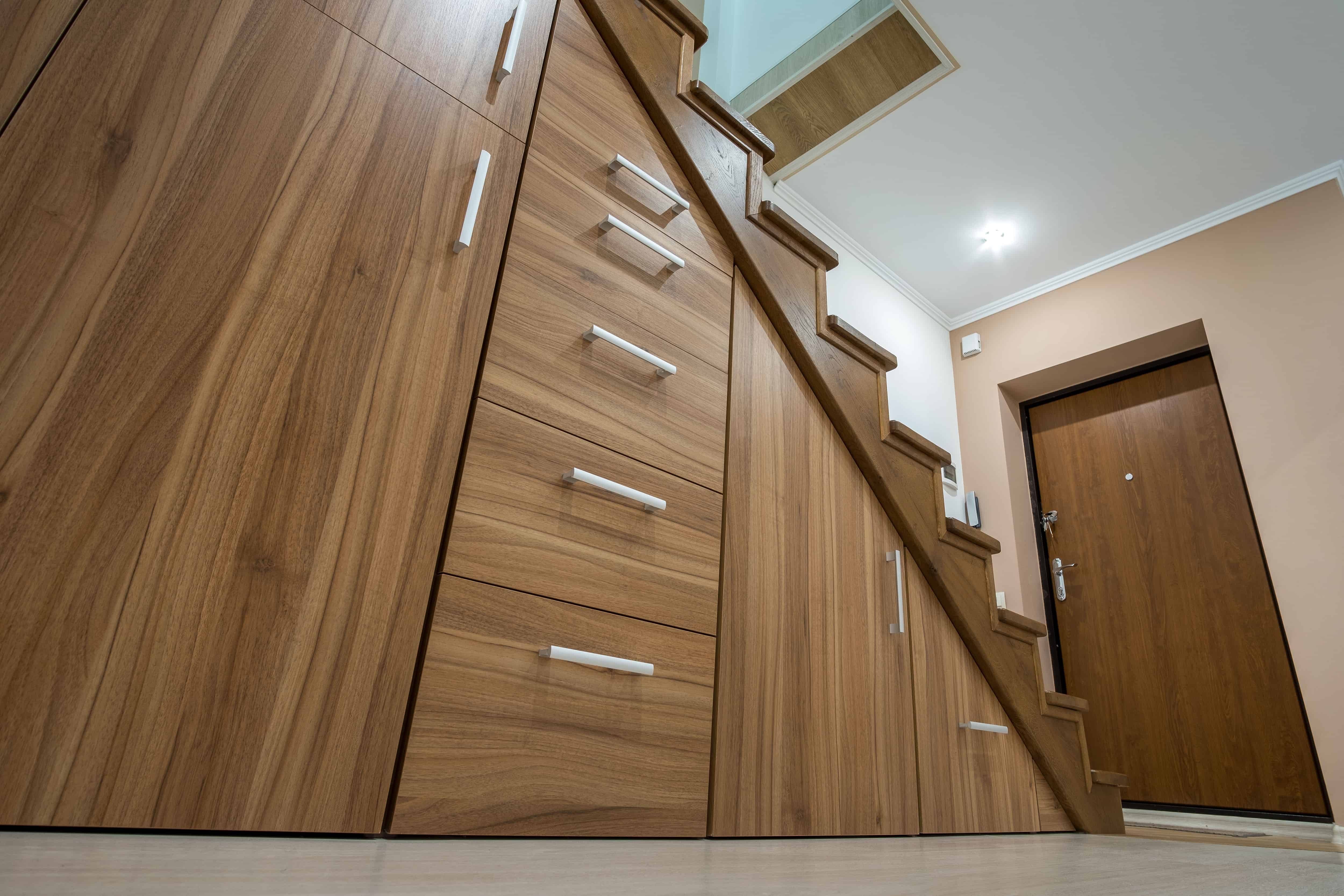 Built-in walnut cabinetry with a row of drawers is tucked beneath a staircase, its brushed metal pulls lined up beside the glass stair railing.