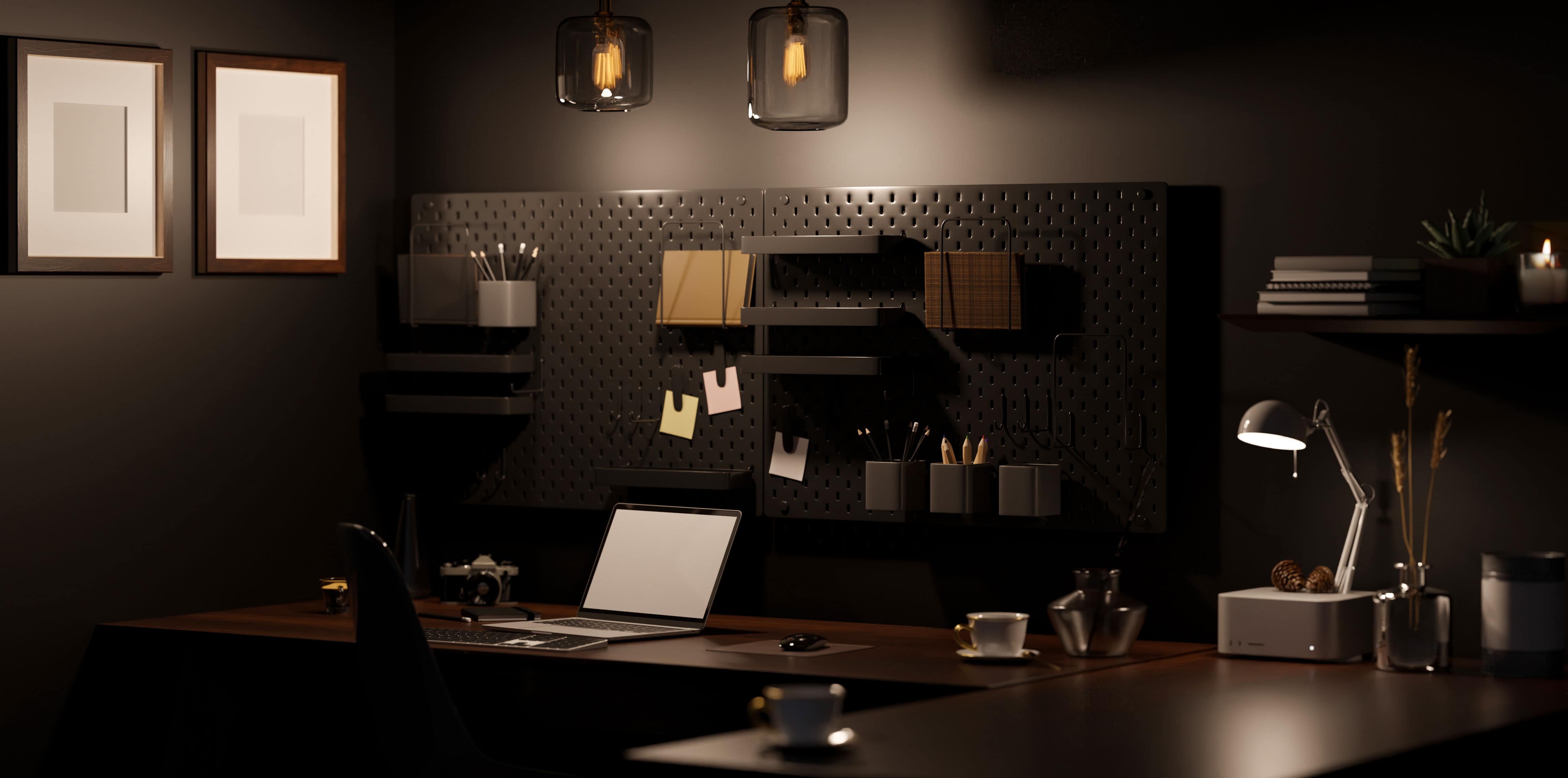 A dark, moody home office work wall with built-in shelving and a wood desk, lit by framed picture lights and a small task lamp.