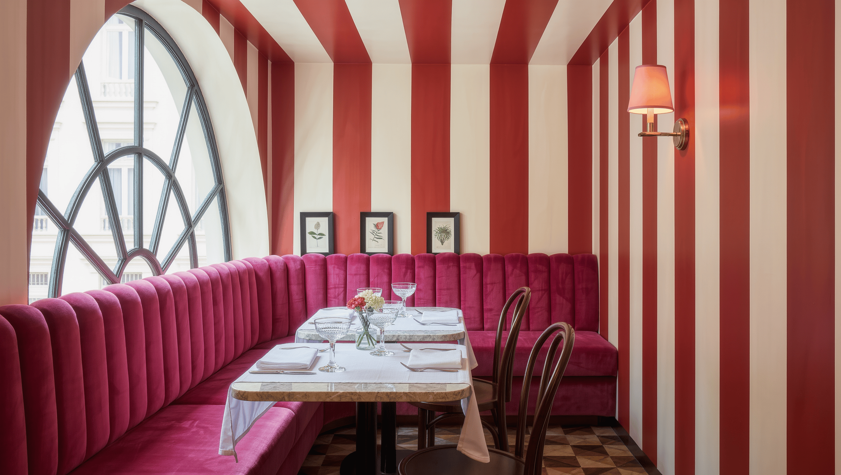 A dining nook with a scalloped fuchsia velvet banquette, marble bistro table, and candy-striped walls in sparkling daylight.