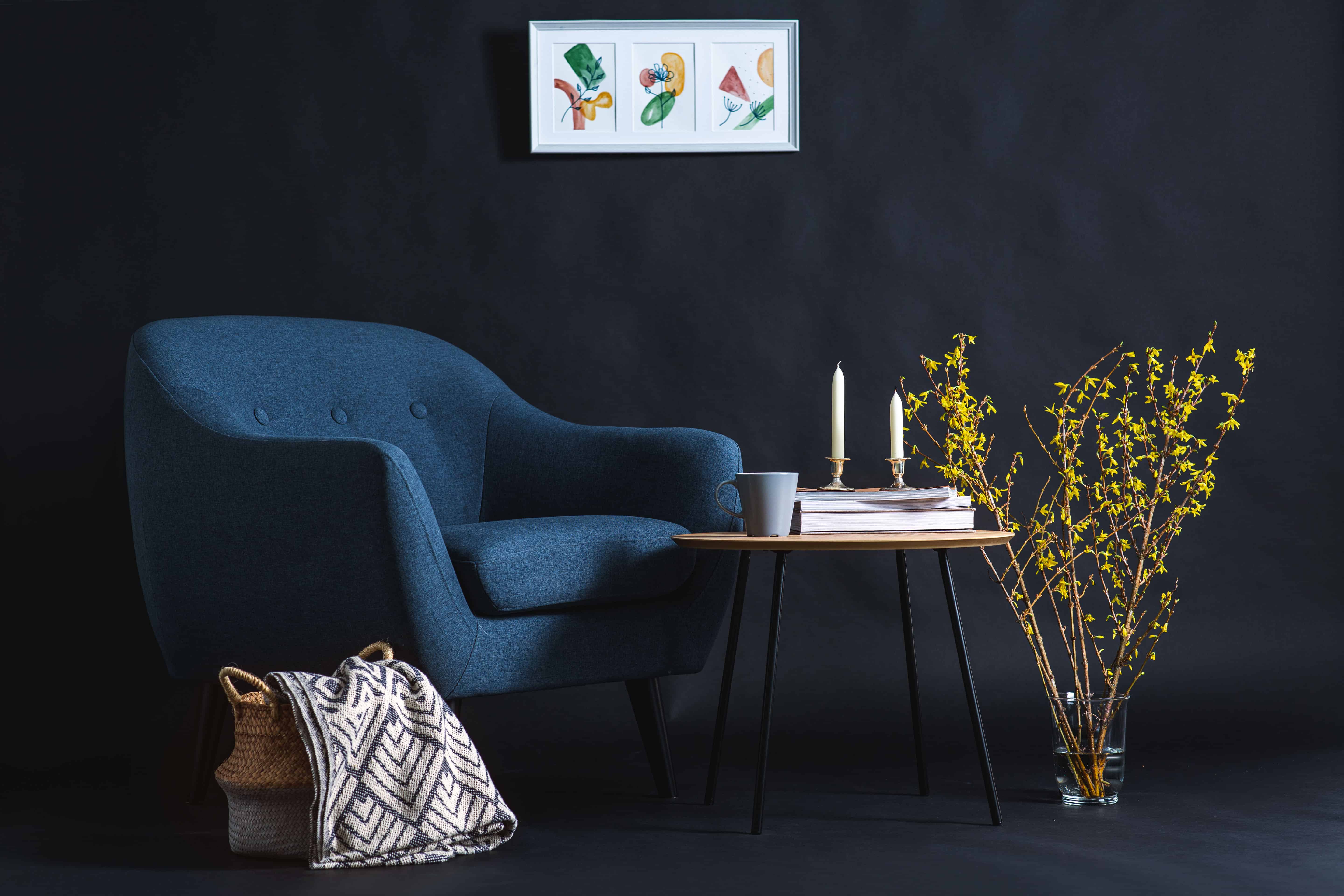 A sapphire velvet armchair beside a woven pet basket and blanket in a moody navy corner, with wildflowers and candlelight nearby.