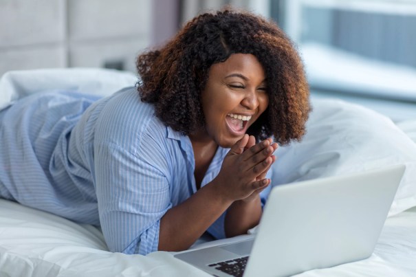 Woman lying on a bed laughing and looking at a computer